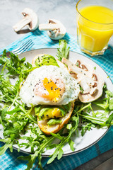 Tasty sandwich with avocado and egg, arugula on concrete background. Delicious breakfast.