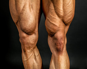 Detail of male bodybuilder front leg muscles on black background. Quadriceps and tibialis anterior.