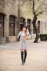 A beautiful girl in a cap is walking around the college. A student is enjoying a spring day. She is wearing sunglasses and a backpack.