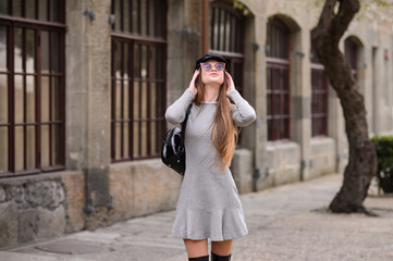 Fototapeta premium A beautiful girl in a cap is walking around the college. A student is enjoying a spring day. She is wearing sunglasses and a backpack.
