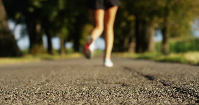 a happy girl fit relaxed jogging and running in a street with trees and nature, using headphones for music and run slow in sunset. concept of happiness for sports and fitness relaxation in nature