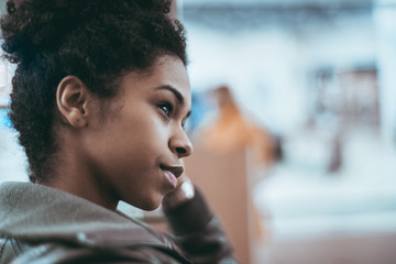 Close-up side view of a young cute Brazilian girl with a curly Afro hair and in a dark-green light...