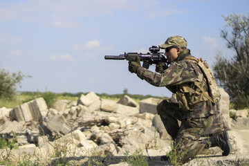 A soldier with a gun , shooting in the sitting position