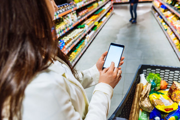 woman hold phone with white screen while make grocery shopping