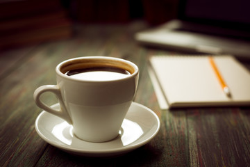 A cup of coffee in the workplace on a wooden table. A cup of coffee in the workplace on a wooden table. The concept of working outside the office