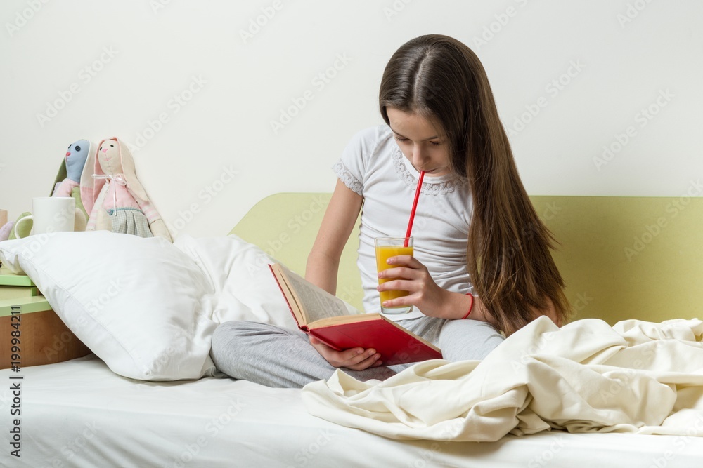 Wall mural teenage girl 10 years old in home clothes reads a book on the bed in her room