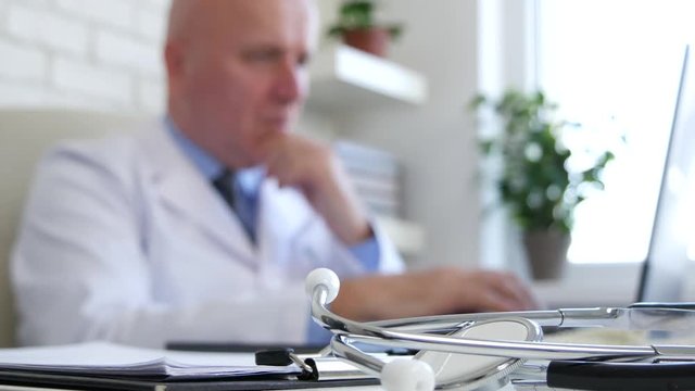 Stethoscope in Focused Image and One Doctor Using Laptop in Blurred Background