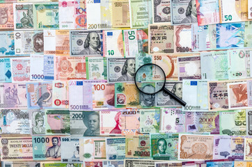 Magnifier on international money banknotes background, top view