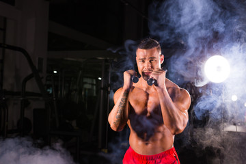 Powerful man doing boxing exercises, making direct hit with dumbbells. Photo of sporty muscular male. Strength and motivation