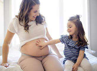 pregnant woman with her daughter on bedroom together