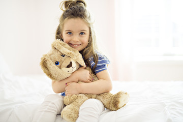 Sweet little girl is hugging a teddy bear on her bed at home