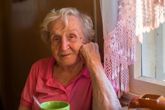 An elderly woman sits at the kitchen table.