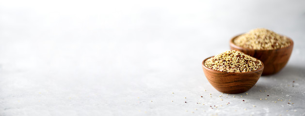 White and red raw organic quinoa in wooden bowl and rosemary on grey background. Healthy food ingredients. Copy space. Banner