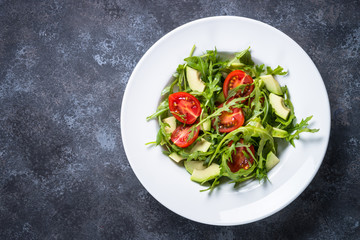 Healthy vegan salad from arugula, avocado and tomatoes.