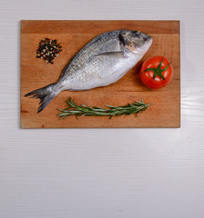 Fresh dorado fish with tomatoe, rosemary lemon and pepper on wooden cutting board
