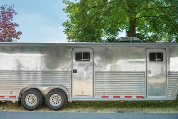 Closeup of a huge silver caravan trailer on a sunny summer day. Might easliy cover horses or cars in addition to the living area.