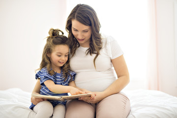 Portrait of a mother and daughter reading a book lying and relax in the bed