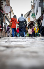 Low down shot of people and couple walking holding hands down a old traditional cobbled English street whilst browsing in shops on retail therapy day