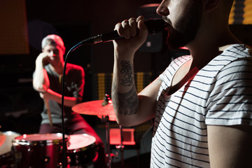 Plakat Side view close up of tattooed hip-hop singer with his music band performing in dim recording studio, copy space