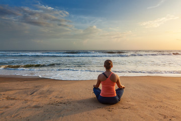 Woman doing yoga oudoors at beach - Padmasana lotus pose