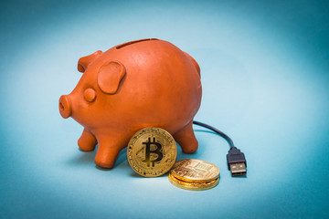 Old piggy bank with bitcoin coins and USB connection with blue background.