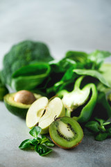 Organic green vegetables and fruits on grey background. Copy space. Green apple, lettuce, cucumber, avocado, kale, lime, kiwi, grapes, banana, broccoli