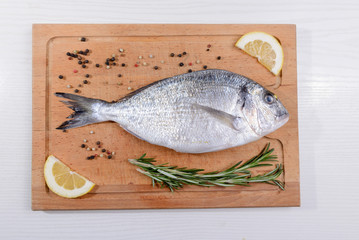 Fresh dorado fish with  rosemary, lemon and pepper on wooden cutting board