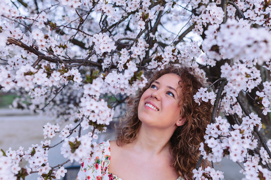 Beautiful curly woman enjoying smell flowering near the cherry tree.