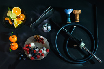 Hookah parts smoking hookah concept at black background isolated with fresh fruits and ice. Hookah bowl, coil, forceps, silicone hose, mounthpiece and kaloud