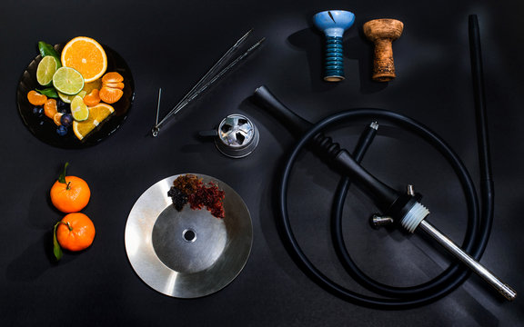 Hookah parts smoking hookah concept at black background isolated with fresh fruits and ice. Hookah bowl, coil, forceps, silicone hose, mounthpiece and kaloud