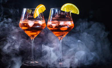 Two glasses of Aperol champagne or cocktails or vine isolated at black background with orange lobule smoke waft party celebration theme