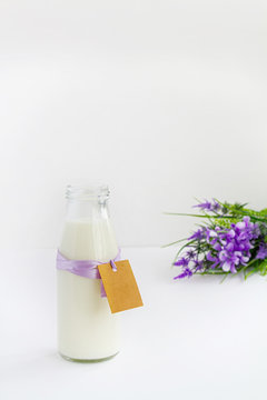 milk bottle with label and inscription Milk is tied with lilac ribbon on wooden light background with lilac flowers.