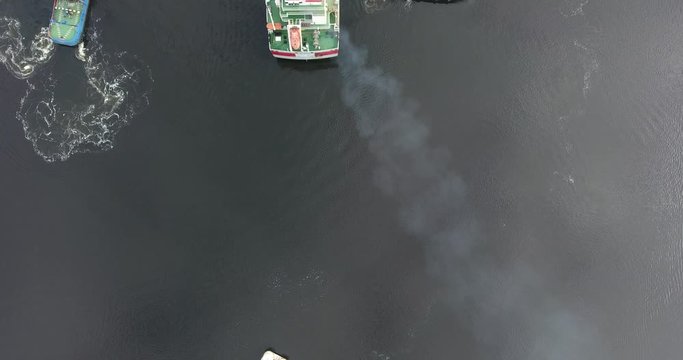 River tug helps when mooring a dry cargo tanker on a calm river early in the morning. Summer day. The camera moves in the air near from the ship. Aerial view.