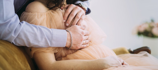Obraz na płótnie Canvas man is hugging pregnant wife sitting on the sofa