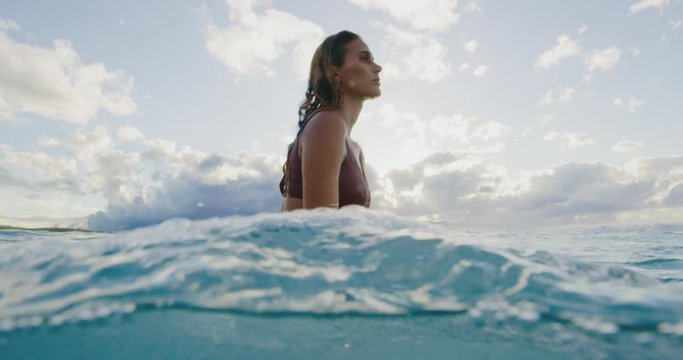 Beautiful young woman surfing at sunset, underwater view
