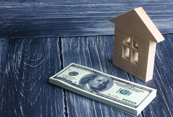 A wooden house stands next to a stack of dolor banknotes. The concept of buying and selling immovability, rent of apartments. Credit and mortgage, affordable housing. Utilities payments.