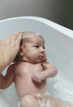 Portrait of relaxed newborn girl in the bathtub with her mother washing her hair