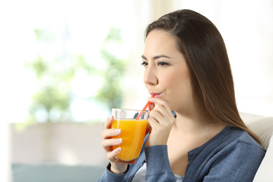 Serious woman drinking orange juice with a straw