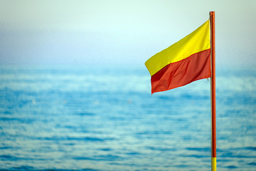 A red and yellow life saving flag against a blue sky