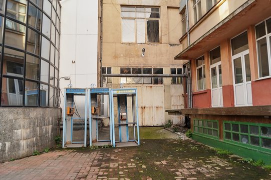 Three old broken phone booths between buildings in a Romanina city