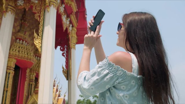 Young woman touirist taking photos while sightseeing Buddhist temple