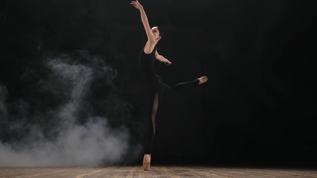 Young beautiful ballerina on smoke stage dancing modern ballet in the dark. Woman in black sexy costume performs on scene. Sensual amazing dance, stretching. Art concept