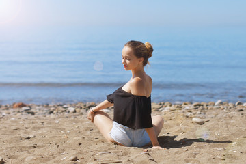 Fototapeta na wymiar Young woman makes meditation in lotus pose on sea / ocean beach, harmony and contemplation. Beautiful girl practicing yoga at sea resort at her vacation. Life style.