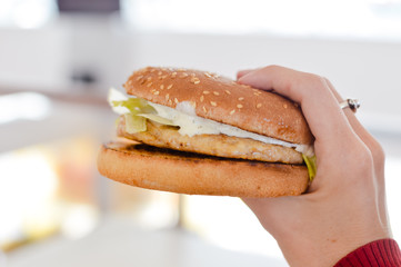 Close up on hand of a person holding a burger on light cooking background. Eating and healthy concept