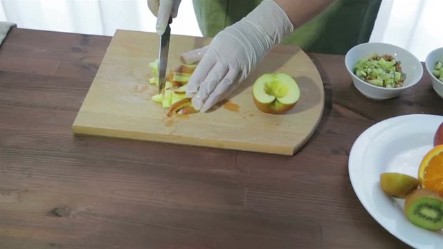 A woman cuts an apple with a knife into slices on a wooden board. The camera moves from right to left.