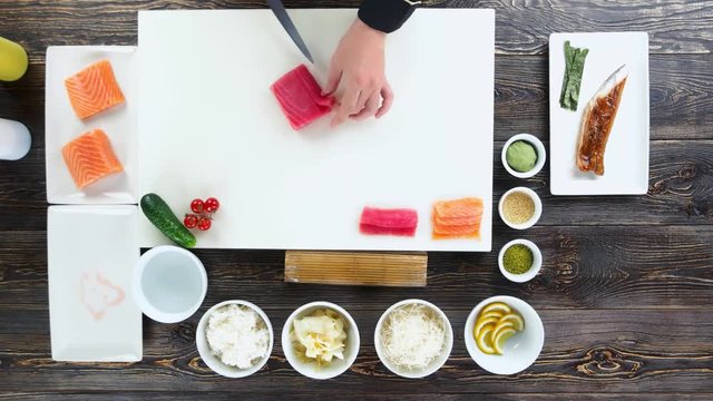Sushi preparation, wooden table. Hands cutting tuna.