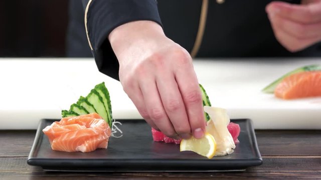 Hands of chef preparing sashimi. Raw fish, ginger and lemon.