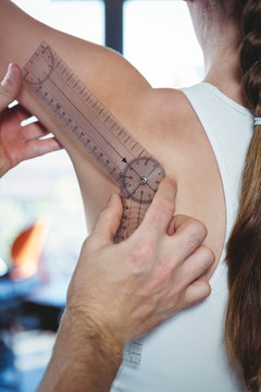 Physiotherapist examining female patient's shoulder with goniometer