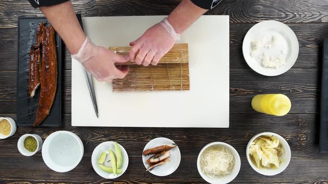 Hands shaping a sushi roll. Japanese food preparation, wooden table.