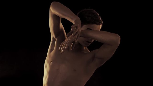 Close up portrait of handsome young ballet dancer with shining golden skin on black background. Body art with gold paint. Fashion man dancing with hands. Slow motion.